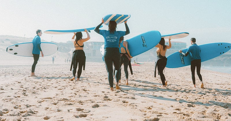 Surfing school class at the beach carrying boards